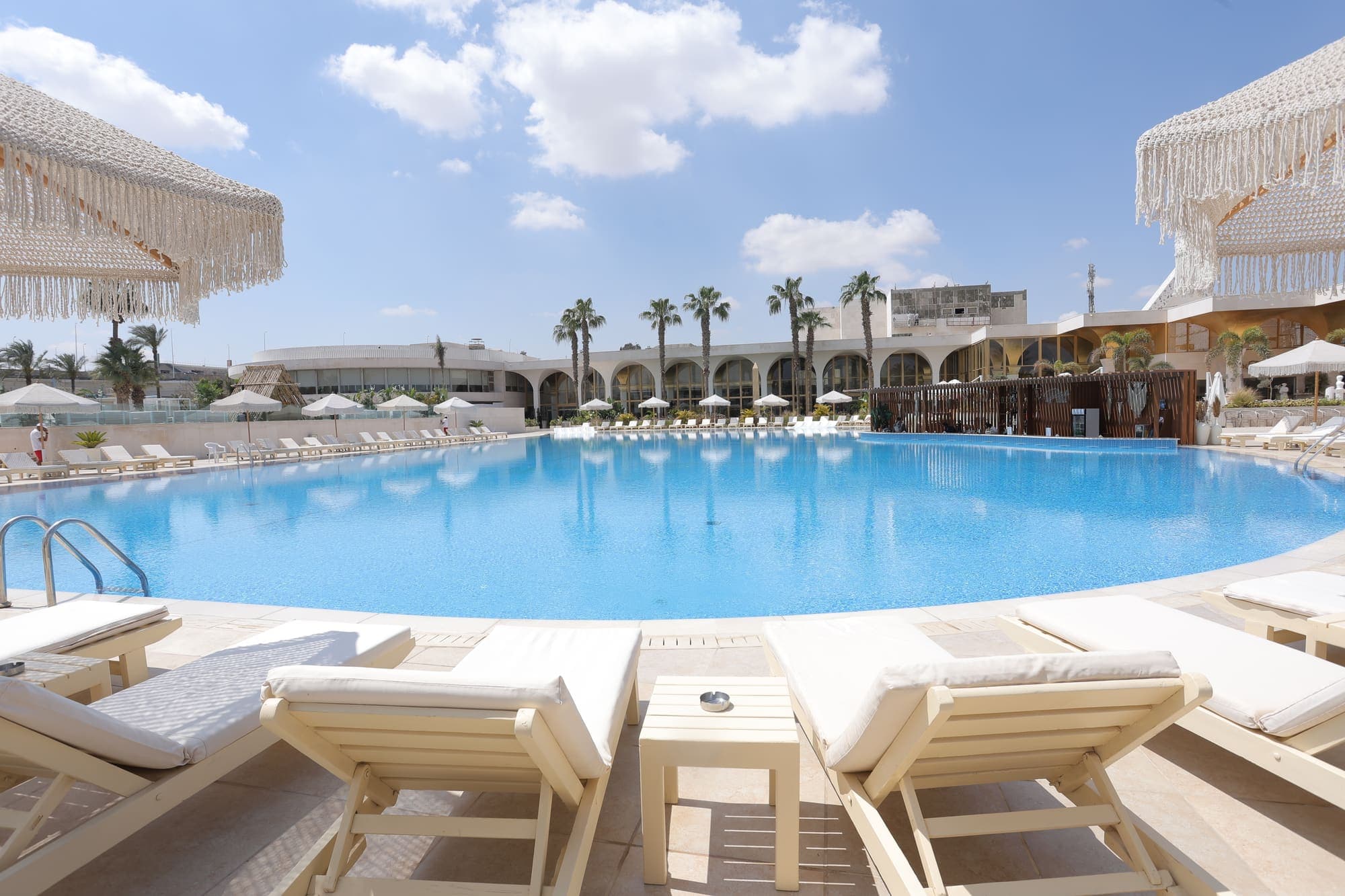 The main pool of the official hotel, fringed with sun loungers and palms